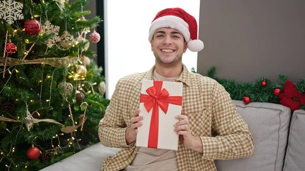 Νεαρός Ισπανός Άνδρας Χαμογελά Σίγουρος Κρατώντας Χριστουγεννιάτικο Δώρο Στο Σπίτι — Φωτογραφία Αρχείου