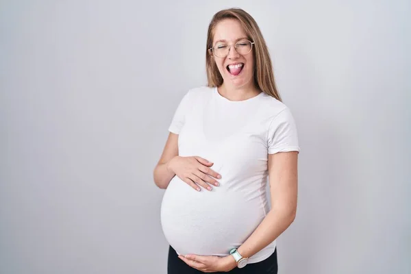 若いです妊娠中の女性は赤ちゃんを期待します 面白い表現で幸せ舌を突き出して妊娠中の腹に触れ — ストック写真