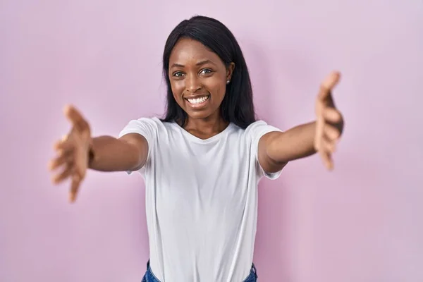 身穿白色休闲衫的非洲年轻女性看着摄像机 张开双臂拥抱对方 欢快的表达拥抱幸福 — 图库照片