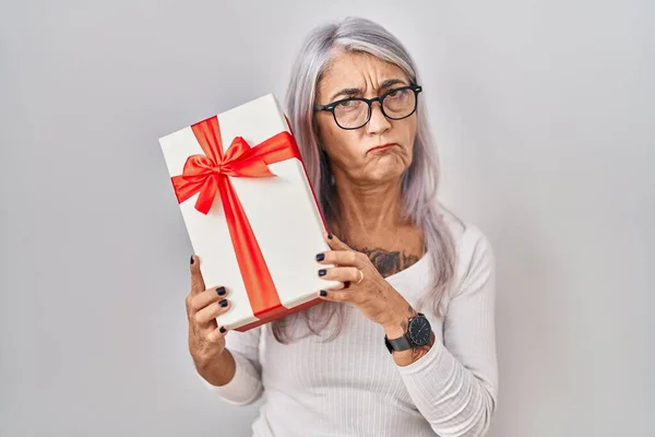 白发苍苍的中年妇女对礼物持怀疑和紧张的态度 皱着眉头因问题而烦恼 消极的人 — 图库照片