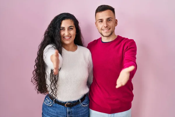 Young Hispanic Couple Standing Pink Background Smiling Friendly Offering Handshake — 스톡 사진
