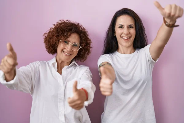 stock image Hispanic mother and daughter wearing casual white t shirt over pink background approving doing positive gesture with hand, thumbs up smiling and happy for success. winner gesture. 