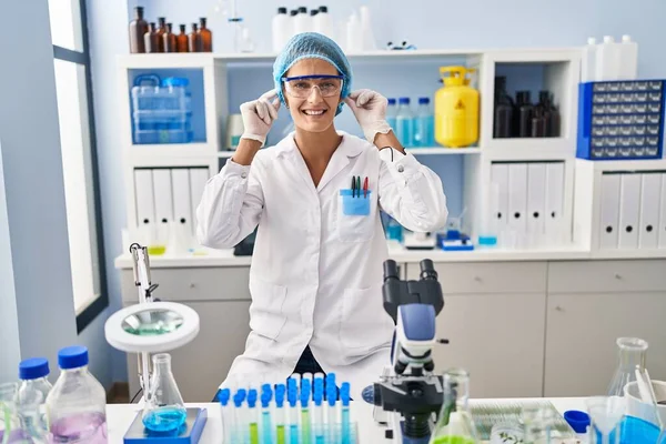 Mujer Morena Trabajando Laboratorio Científico Sonriendo Tirando Las Orejas Con —  Fotos de Stock
