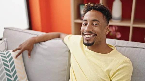 アフリカ系アメリカ人の男は自信を持って笑顔でソファに家に座って — ストック写真