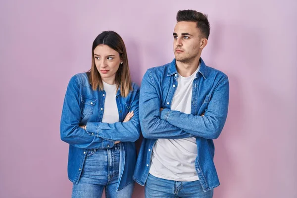 Young Hispanic Couple Standing Pink Background Looking Side Arms Crossed — Stock Photo, Image