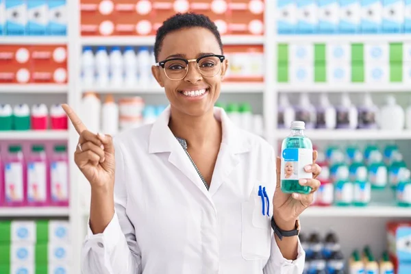 Африканская Американка Работающая Аптеке Держит Сироп Улыбаясь Показывая Рукой Пальцем — стоковое фото