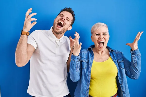 年轻的巴西母亲和儿子站在蓝色的背景上庆祝疯狂和疯狂的成功 他们举起双臂 闭上眼睛 兴奋地尖叫着 获奖者概念 — 图库照片