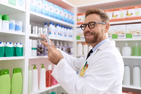 薬局で読書処方の棚に製品を保持する中年男性薬剤師 — ストック写真