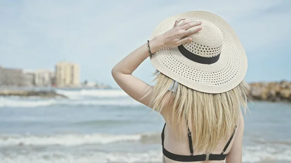 若いですブロンド女性観光客身に着けていますビキニと夏帽子立って後方にビーチ — ストック写真