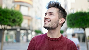 Young hispanic man smiling confident looking to the side at street