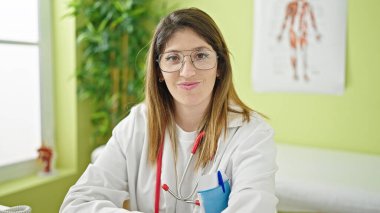 Genç sarışın doktor klinikte gözlük takarak gülümsüyor.