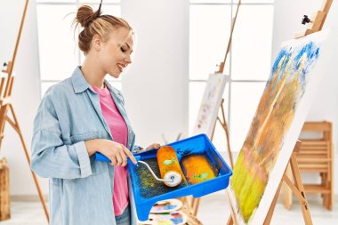 Resim stüdyosunda boya silindiri kullanan genç beyaz kadın sanatçı.