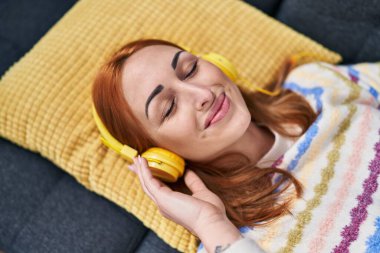 Young caucasian woman listening to music lying on sofa at home