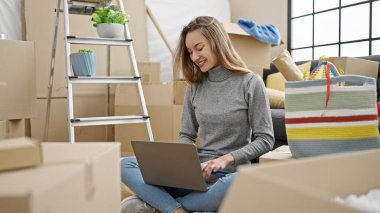 Young caucasian woman using laptop sitting on floor at new home