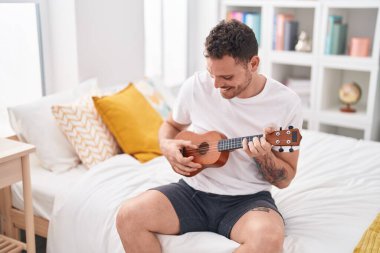 Genç İspanyol adam yatakta ukulele oynuyor.