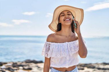 Genç Afrikalı Amerikalı kadın turist, gülümsüyor. Deniz kenarında akıllı telefondan konuşuyor.