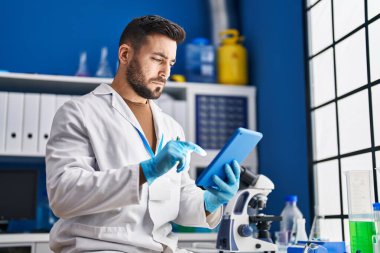 Laboratuvarda dokunmatik ped kullanan genç bir İspanyol bilim adamı üniforması giyiyor.