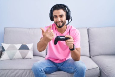 İspanyol genç adam video oyunu oynuyor. Kanepede oturmuş seni bekliyor. Gel buraya. 