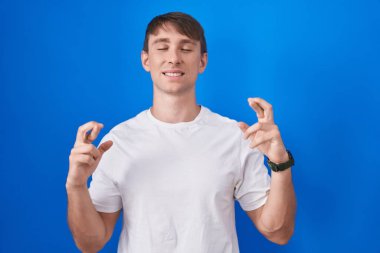 Beyaz, sarışın bir adam mavi arka planda duruyor. Umut ve gözler kapalı bir şekilde gülümseyerek işaret ediyor. Şans ve batıl inançlar. 