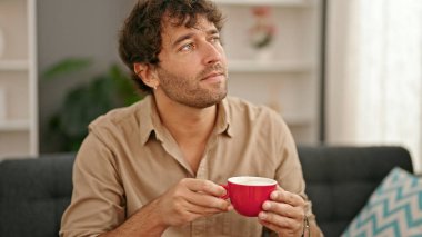 Genç İspanyol adam evdeki kanepede kahve içiyor.