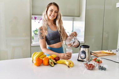Young woman smiling confident pouring smoothie on glass at kitchen