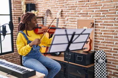 Müzik stüdyosunda keman çalarken gülümseyen Afrikalı Amerikalı kadın müzisyen.
