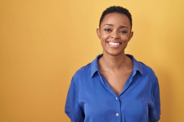 Yüzünde mutlu ve havalı bir gülümsemeyle sarı arka planda duran Afrikalı Amerikalı kadın. şanslı kişi. 