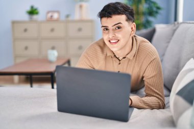 Evdeki kanepede dizüstü bilgisayar kullanan genç bir adam.
