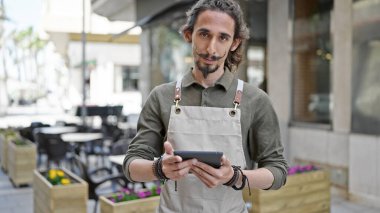 Genç İspanyol garson, kahve dükkanının terasında ciddi yüzlü dokunmatik ped kullanıyor.
