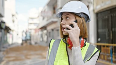 Sarışın genç bir mimar sokakta akıllı telefondan konuşuyor.