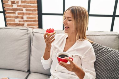 Genç İspanyol kadın evdeki kanepede kahvaltı yapıyor.