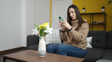 Evdeki kanepede oturmuş vazoda çiçeklerin fotoğrafını çeken güzel İspanyol kadın.