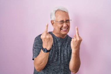 Middle age man with grey hair standing over pink background showing middle finger doing fuck you bad expression, provocation and rude attitude. screaming excited  clipart