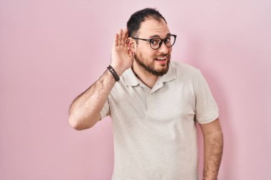 Artı, pembe arka planda duran sakallı, ağzı kulaklarında dedikoduları ve dedikoduları dinleyen İspanyol bir adam. Sağırlık kavramı. 