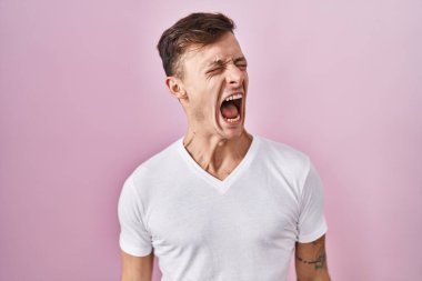 Caucasian man standing over pink background angry and mad screaming frustrated and furious, shouting with anger. rage and aggressive concept. 