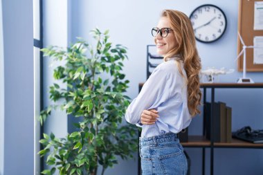 Sarışın, genç bir iş kadını, kollarını kavuşturup ofiste el kol hareketi yapıyor.