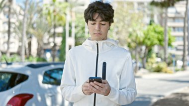 Genç İspanyol bir adam parkta akıllı telefon kullanıyor.