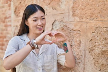 Çinli kadın gülümseyerek kalp hareketi yapıyor. Sokakta elleriyle.