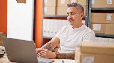 Ofiste dizüstü bilgisayar kullanan Latin asıllı genç bir iş adamı.