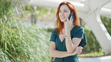 Young redhead woman smiling confident talking on the smartphone at park