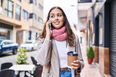Young beautiful hispanic woman using smartphone drinking coffee at street