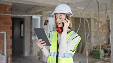 Şantiyede akıllı telefondan konuşan genç sarışın mimar.