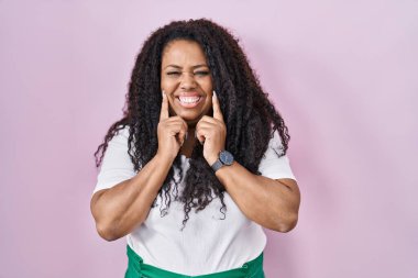 Artı, pembe arka planda duran, ağzı açık gülümseyen, parmakları işaret eden ve neşeli gülümsemeye zorlayan İspanyol kadın. 