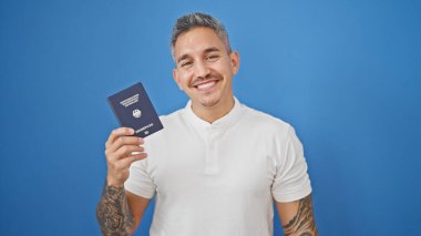 Genç İspanyol adam gülümsüyor. Kendine güveni tam. Hollanda pasaportu izole edilmiş mavi arka planda.