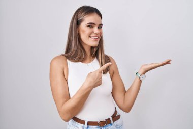 Beyaz arka planda duran Latin kökenli genç kadın kameraya hayret ediyor ve gülümsüyor.. 