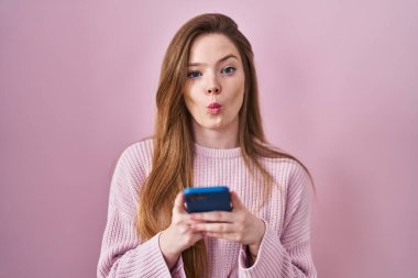 Kafkasyalı genç bir kadın akıllı telefon kullanıyor. Mesaj yazıyor. Ağızlı balık suratı ve şaşı gözler yapıyor.. 