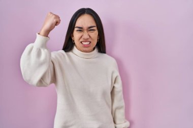 Pembe arka planda duran genç Güney Asyalı kadın kızgın ve kızgın yumruğunu kaldırıyor ve öfkeyle bağırıyor. öfke ve agresif konsept. 