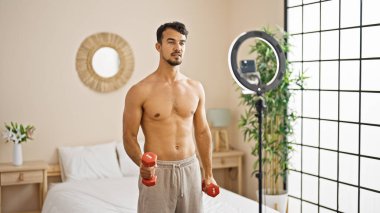 Genç İspanyol adam yatak odasında dambıllarla çevrimiçi eğitim alıyor.