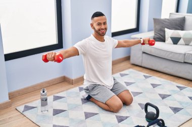 African american man smiling confident using dumbbells training at home