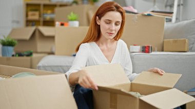 Genç kızıl saçlı kadın yeni evinde bavulunu açıyor.